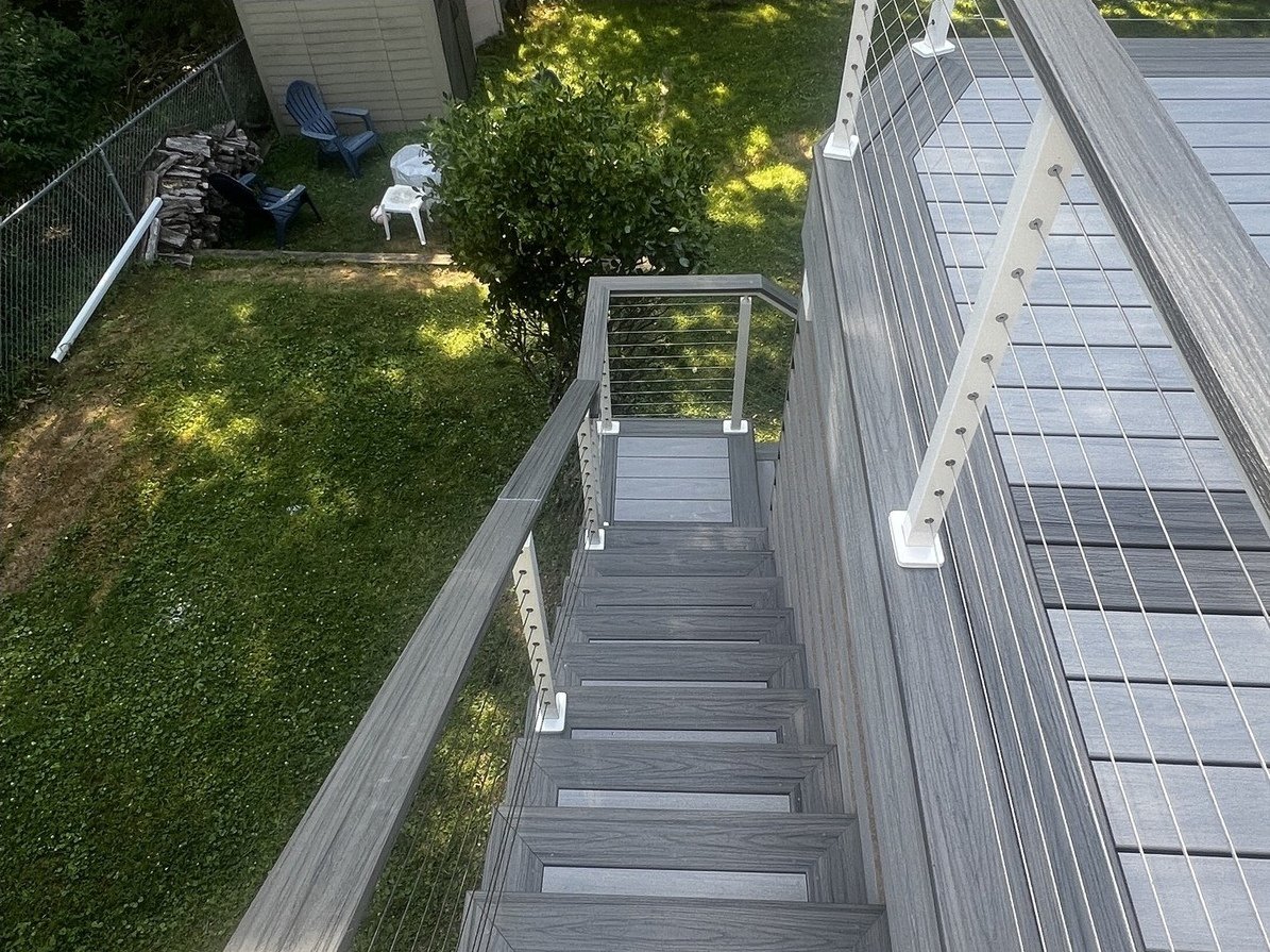 View down the deck stair with cable railing and the yard below.